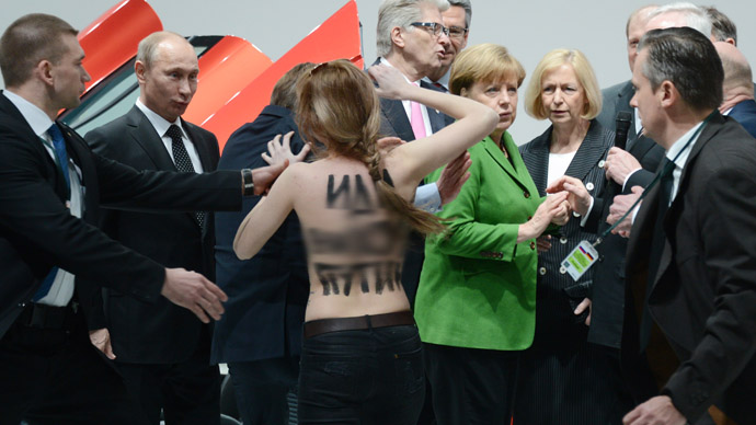 A topless demonstrator with a message on her back walks towards Russian President Vladimir Putin (L) and German Chancellor Angela Merkel (C) during their visit of the Hanover industrial Fair in Hanover, central Germany, on April 8, 213. Four bare-breated demonstrators shouted "fuck dictator"at Russian President Vladimir Putin as he was visiting the Volkswagen stand.   AFP PHOTO / Jochen Lьbke +++ GERMANY OUT