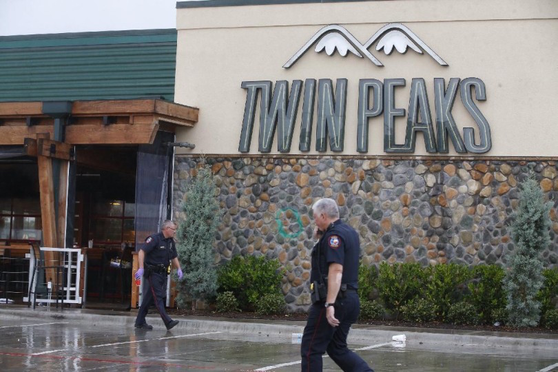 Waco police officers walk along the perimeter of Twin Peaks restaurant during an investigation Wednesday, May 20, 2015 in Waco, Texas.  A deadly weekend shootout involving rival motorcycle gangs apparently began with a parking dispute and someone running over a gang member's foot, police said Tuesday.  (Rod Aydelotte/Waco Tribune Herald, via AP)